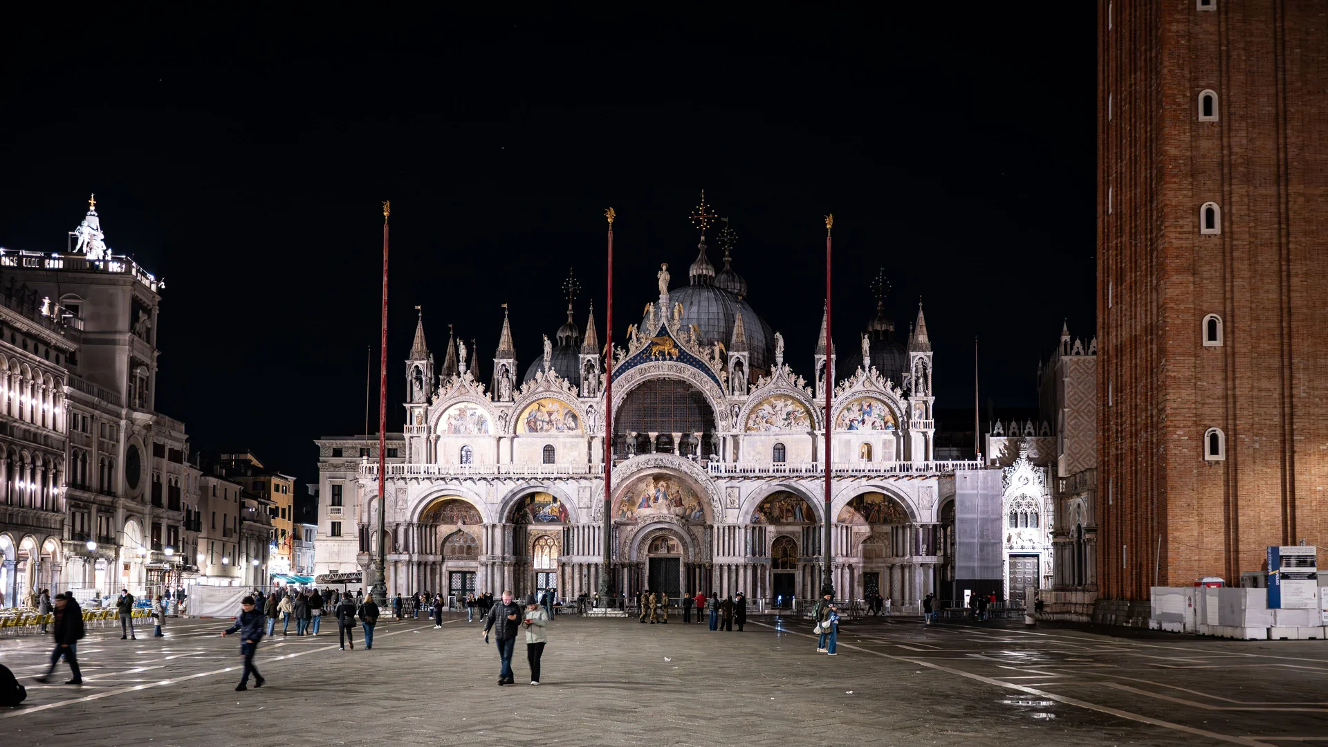 St Mark's Basilica osvětlená v noci, její mozaiková fasáda zářící zlatem nad téměř prázdným náměstím Piazza San Marco